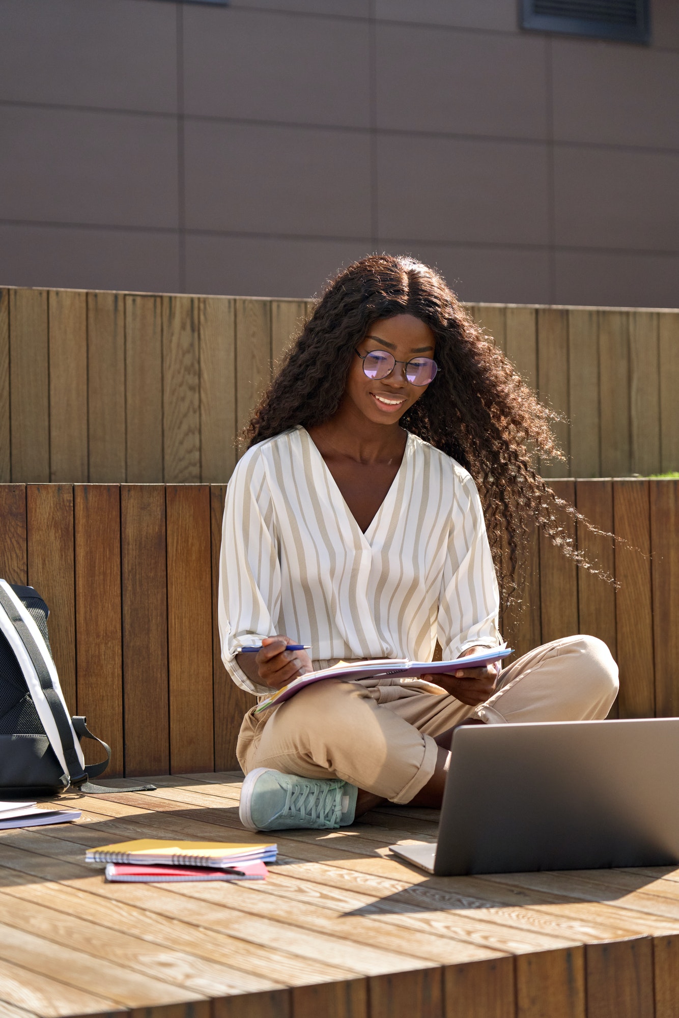 Happy African girl student elearning using laptop studying outside.